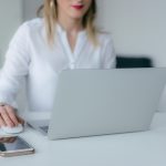 A woman working at a desk using a laptop and smartphone, exemplifying remote work.